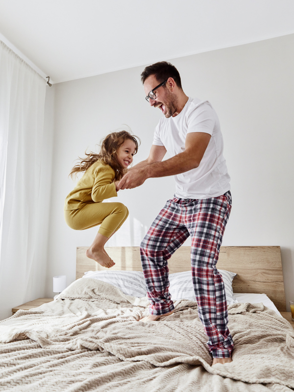 Ein Vater springt mit seiner Tochter gemeinsam auf dem Bett.